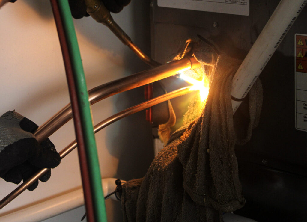 close-up view of technician using cutting torch on copper piping