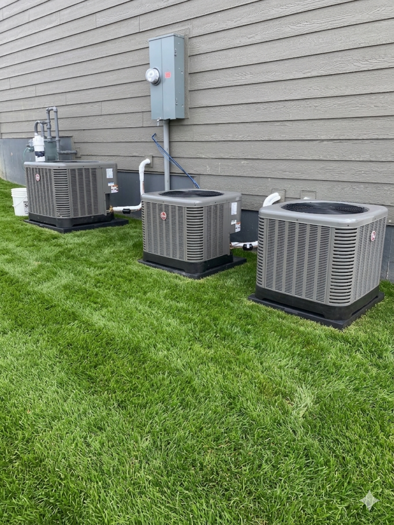 three air conditioners installed next to home with green lawn