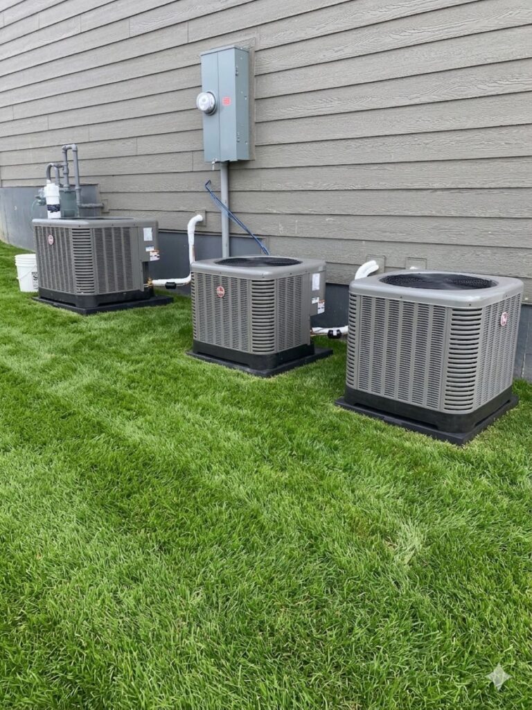 Three residential air-conditioning condenser units installed beside a home.